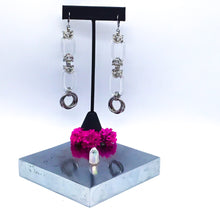 Load image into Gallery viewer, Two Long Krystal earrings side by side. Center focus is two large transparent rings, held together by handmade stainless steel chainmaille weaves. Finished with 2 woven large stainless steel rings.