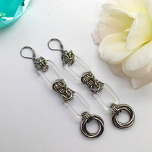 Load image into Gallery viewer, Two Long Krystal earrings side by side. Center focus is two large transparent rings, held together by handmade stainless steel chainmaille weaves. Finished with 2 woven large stainless steel rings.